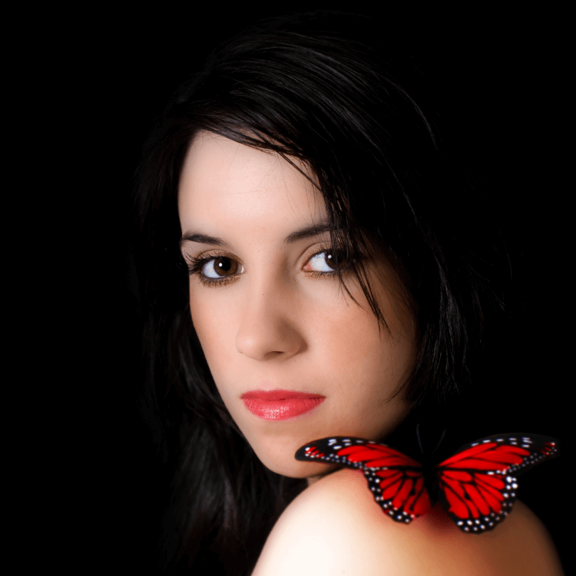 Mujer con labios cautivadores y mariposa roja en el hombro, mostrando belleza y elegancia.